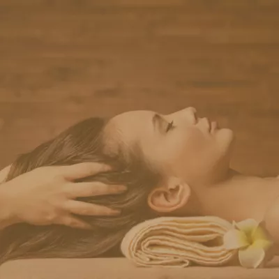 Woman receiving scalp massage at spa, with rolled towel and frangipani flower beside her